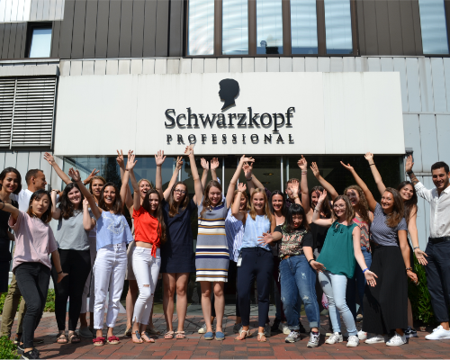 Une équipe diversifiée de Henkel applaudissant devant le bâtiment professionnel Schwarzkopf et levant les bras