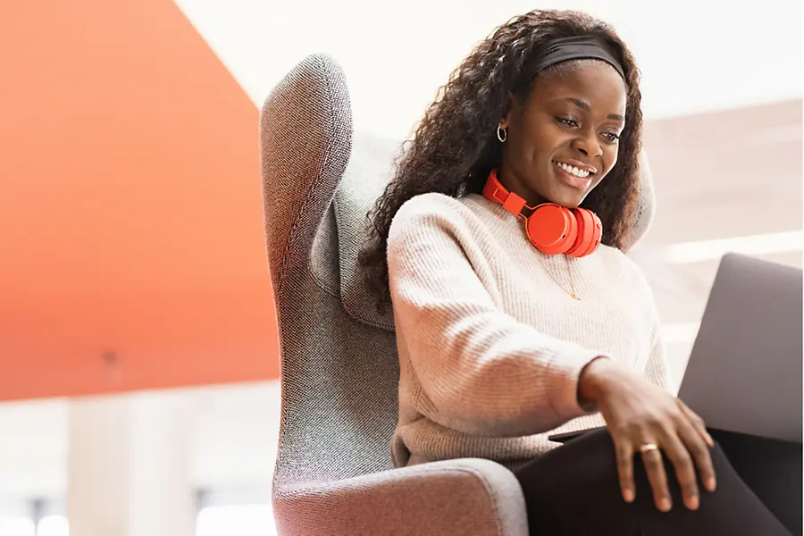 Une employée de Henkel est assise dans un fauteuil confortable avec son ordinateur portable sur les genoux. Elle sourit. 