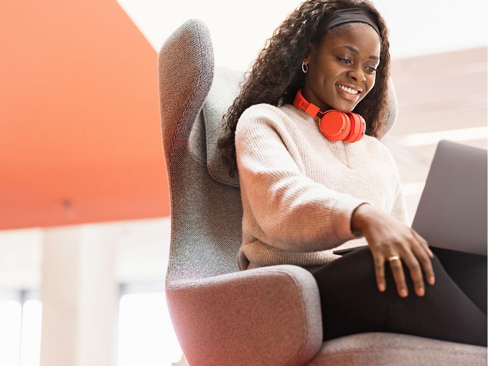Une employée de Henkel est assise dans un fauteuil confortable avec son ordinateur portable sur les genoux. Elle sourit. 