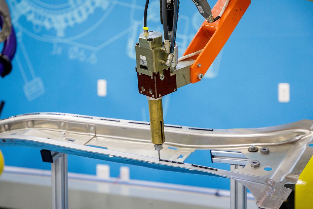 Robotic arm applying adhesive to section of car body