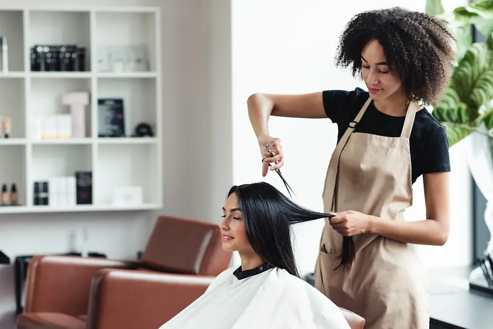 Female hairdresser cutting a woman’s hair in a light salon space.