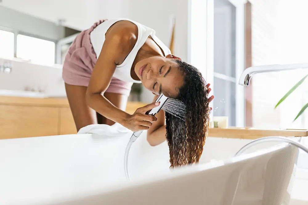Femme dans une salle de bain lavant ses cheveux bruns dans un tube de bain