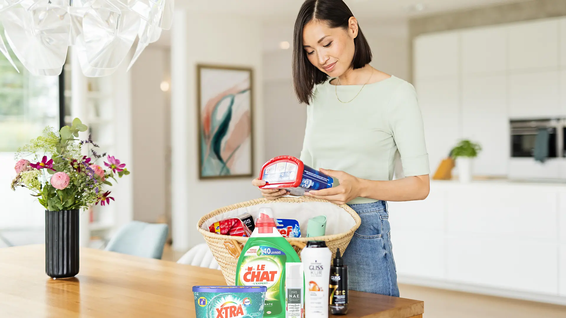 Femmes avec un panier sur une table remplie de produits Henkel tels que : Le Chat, Gliss, Bref, Somat, taft. et plus encore.