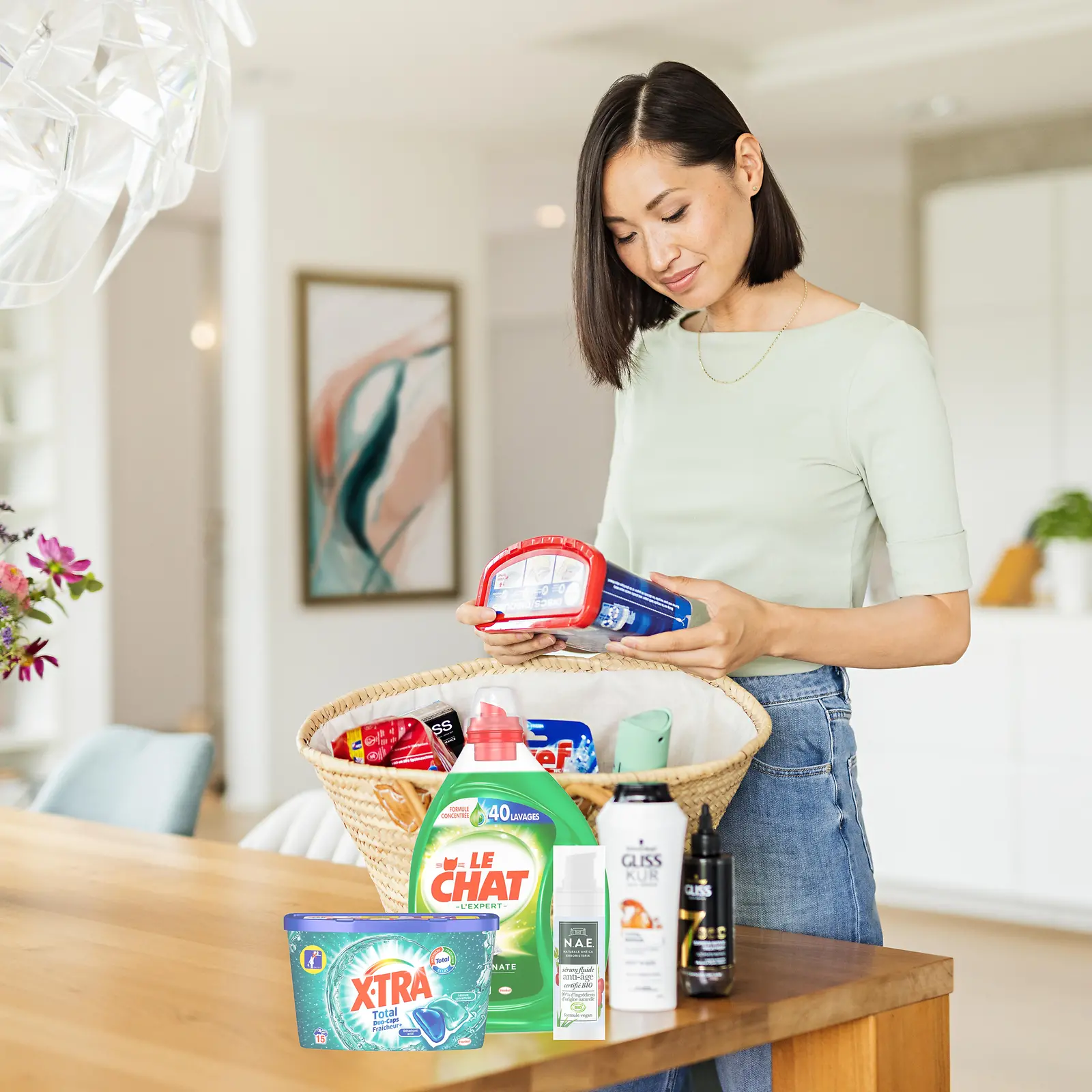 Femmes avec un panier sur une table remplie de produits Henkel tels que : Le Chat, Gliss, Bref, Somat, taft. et plus encore.