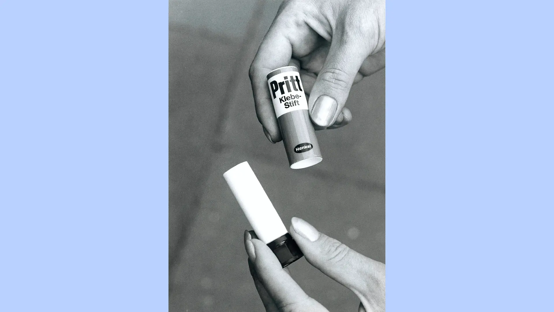 Photo en noir et blanc montrant des mains tenant un bâton de colle Pritt ouvert. La main droite tient le capuchon tandis que la main gauche tient la partie avec le mécanisme rotatif.