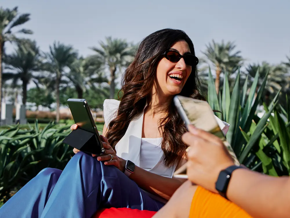 Une femme travaillant sur un ordinateur portable en plein air dans un parc ensoleillé, reflétant les options de travail flexibles et la culture de travail moderne de Henkel.