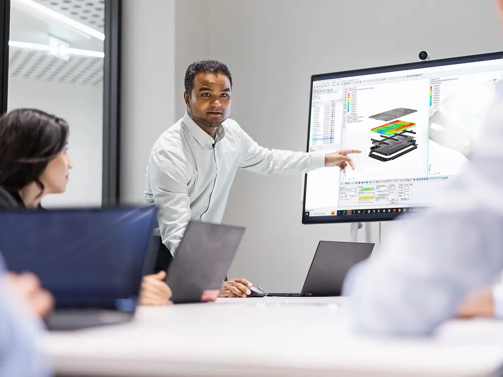 Une équipe collabore à l'innovation en utilisant les solutions Loctite, avec un professionnel qui présente des conceptions de modélisation et de simulation sur un grand écran lors d'une réunion technique.