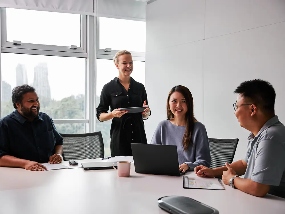 Un groupe diversifié de professionnels dans une salle de réunion moderne, collaborant autour d'une table avec des ordinateurs portables et des documents. La scène reflète l’engagement de Henkel en faveur de la parité des genres et de la diversité au sein de la direction, mettant en avant un environnement de travail inclusif où différentes perspectives contribuent à la prise de décision.