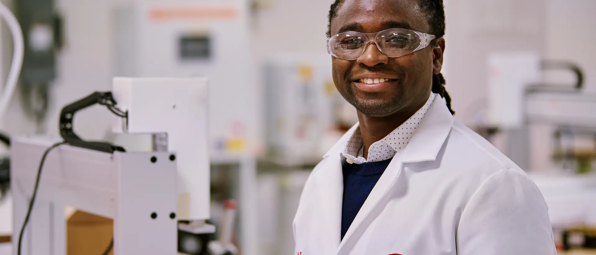 Une personne portant une blouse de laboratoire blanche Henkel, debout dans un environnement de laboratoire, entourée d’équipements et de machines.