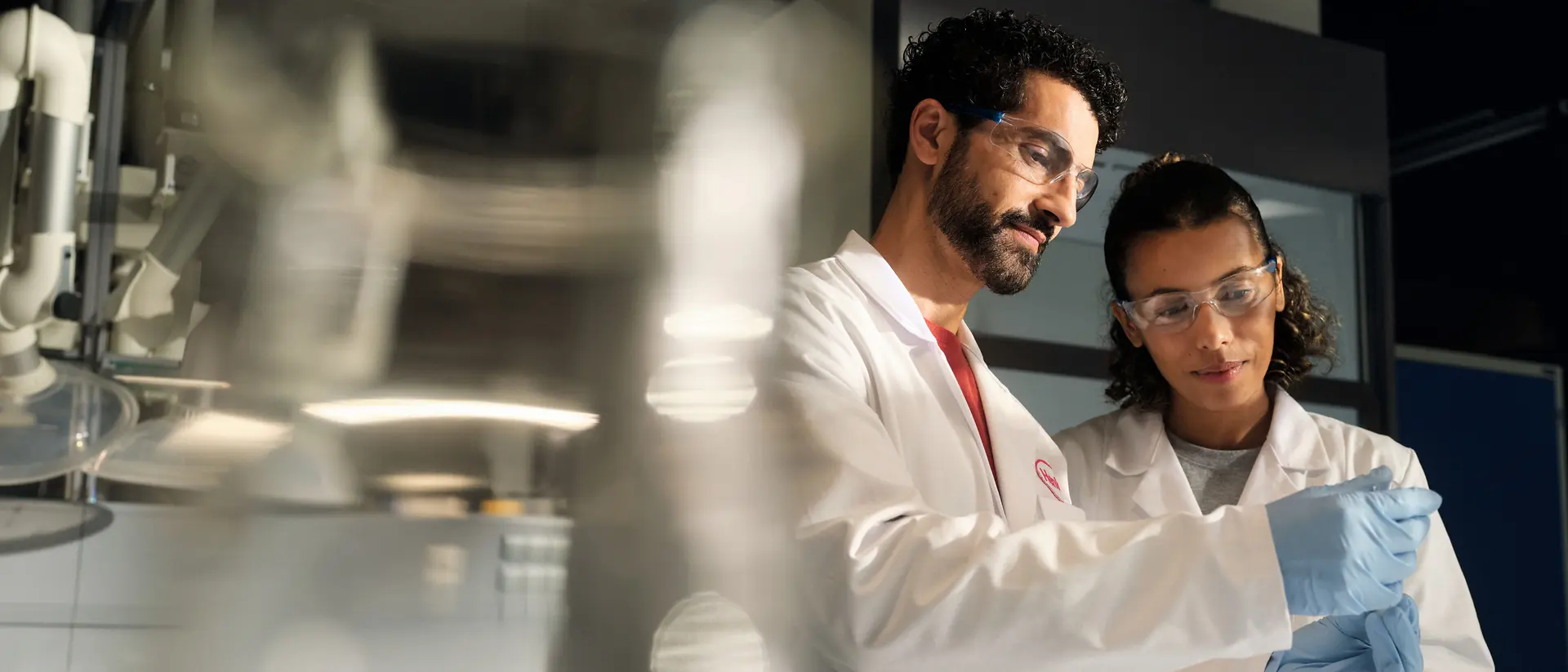 Deux scientifiques portant une blouse blanche, des gants de sécurité, examinant un échantillon dans un laboratoire.